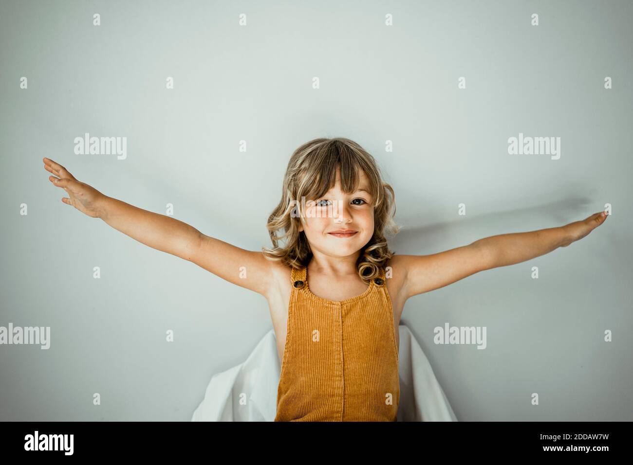 Petite fille avec les bras tendus debout contre le mur à la maison Banque D'Images