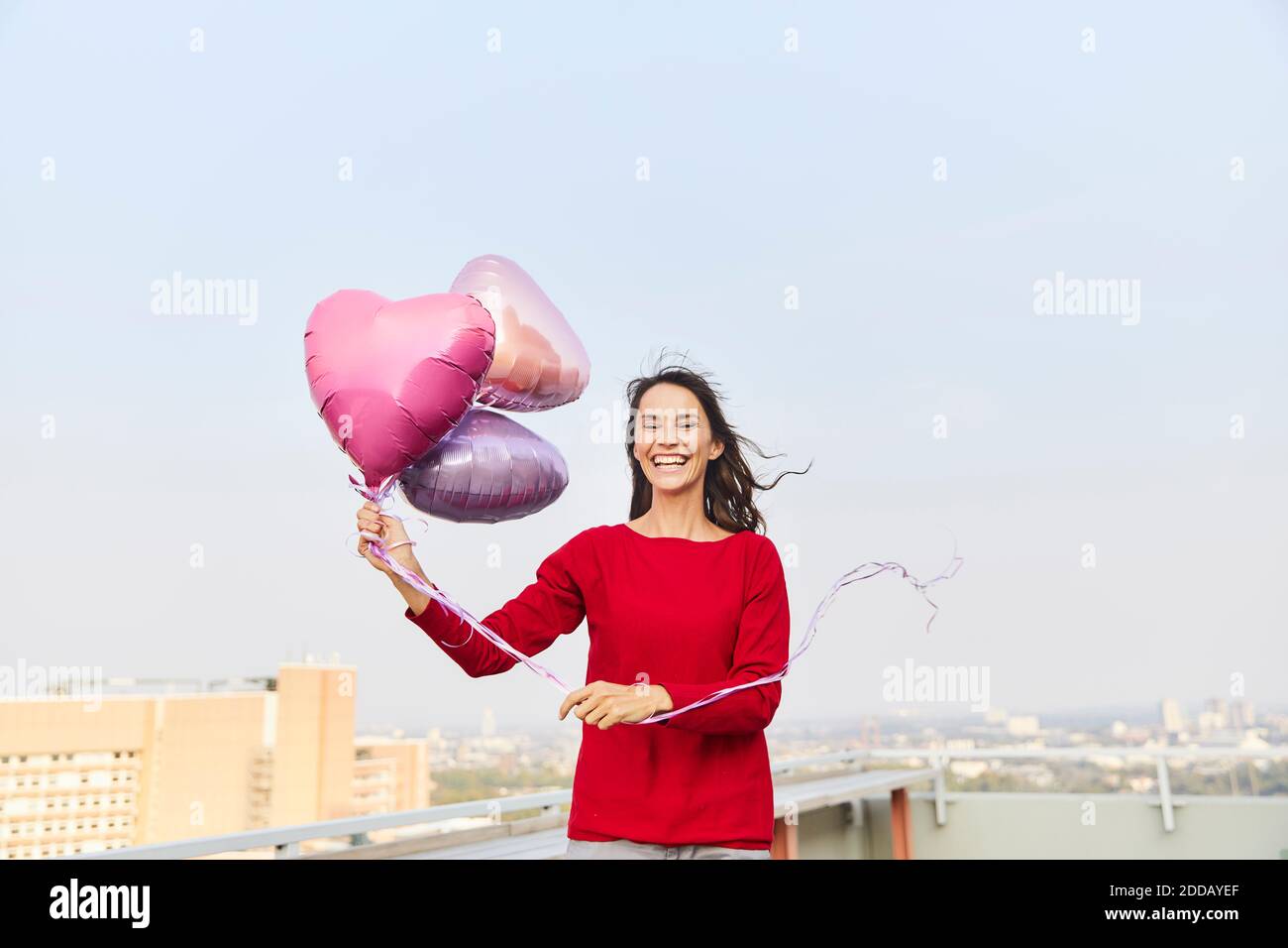 Femme mûre tenant un ballon en forme de coeur tout en étant debout sur le bâtiment terrasse au ciel clair Banque D'Images