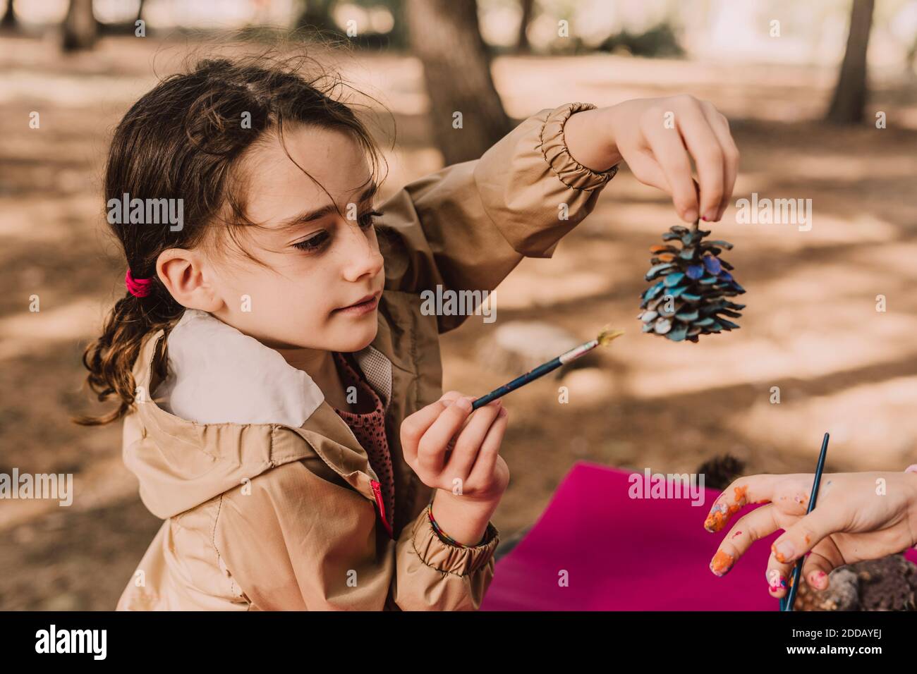 Jolie fille tenant le cône de pin tout en colorant par soeur à stationnement Banque D'Images