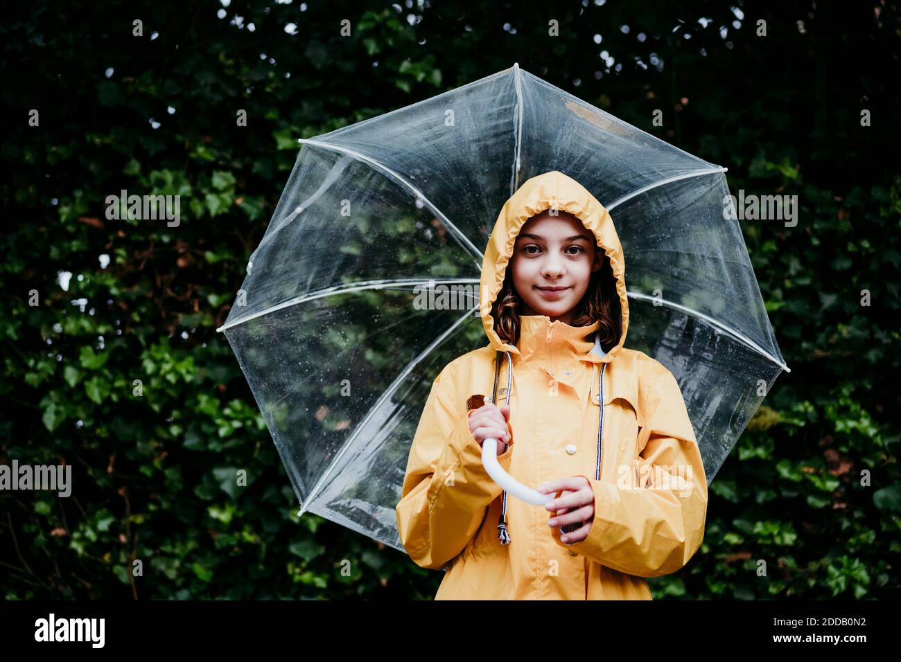 Fille portant un imperméable tenant un parapluie tout en se tenant contre le mur des feuilles Banque D'Images