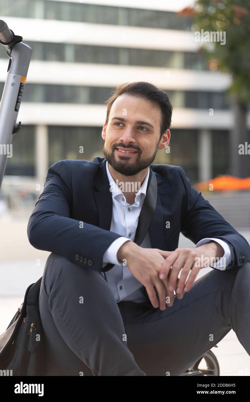 Homme d'affaires souriant en scooter électrique assis en ville Banque D'Images