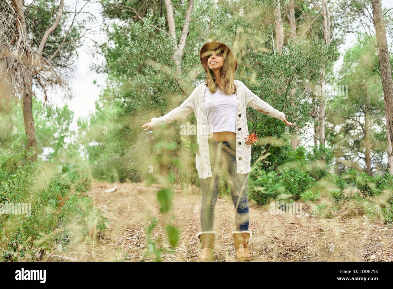 Femme regardant loin en se tenant debout avec les bras débordés au milieu des plantes et arbres en forêt Banque D'Images