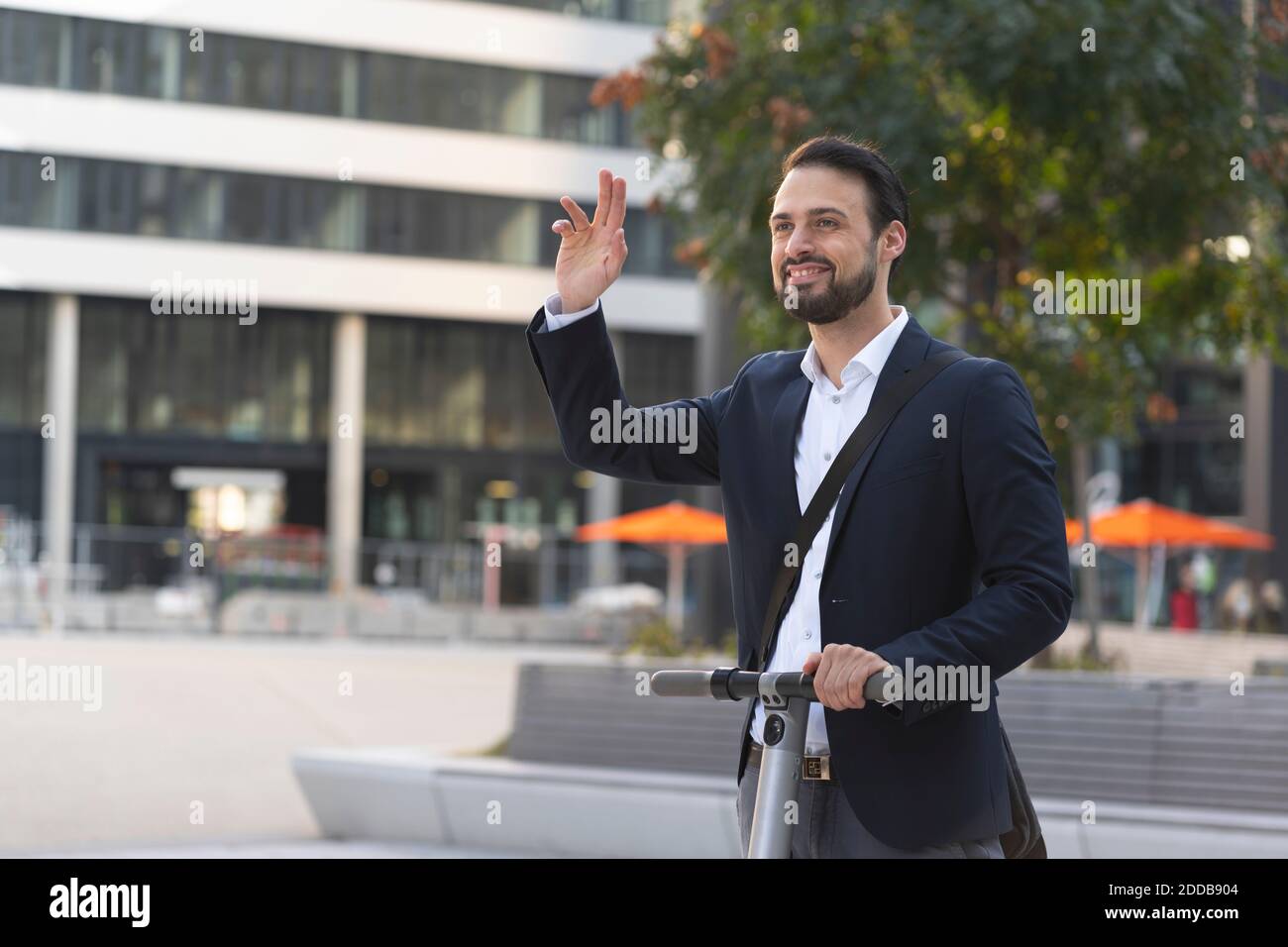 Homme d'affaires souriant qui agite sur un scooter électrique en ville Banque D'Images