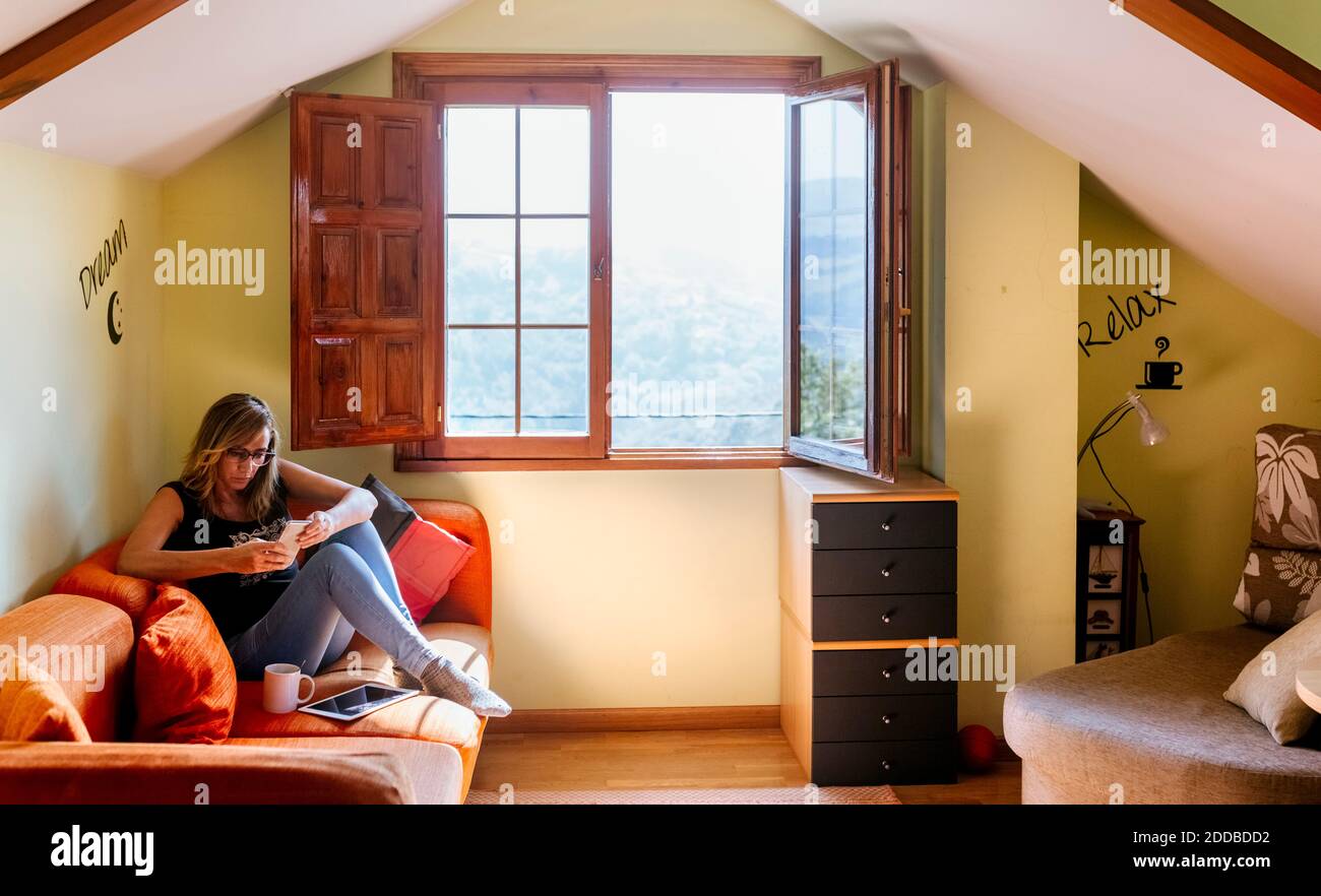 Mature Woman using smart phone while sitting on sofa at home Banque D'Images