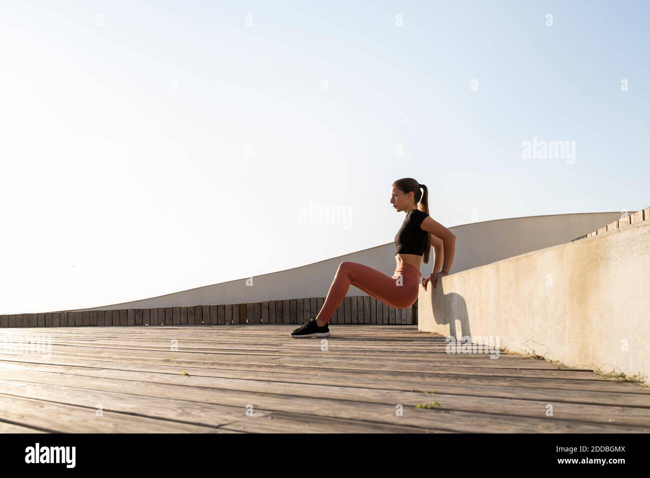 Athlète féminine faisant la position de presse de banc sur la promenade contre clair ciel Banque D'Images
