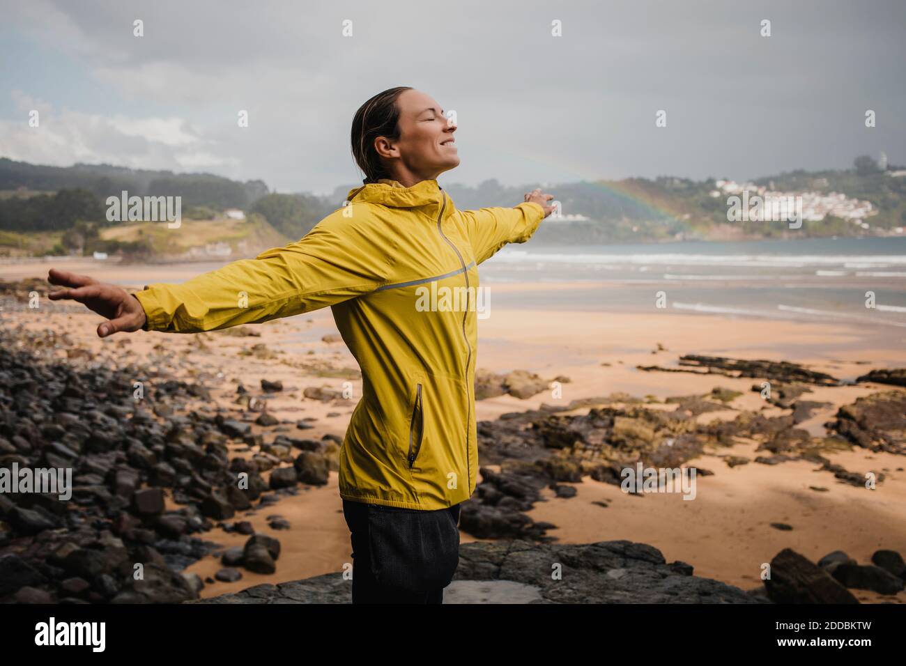 Femme souriante en imperméable jaune à la plage pendant la saison des pluies Banque D'Images