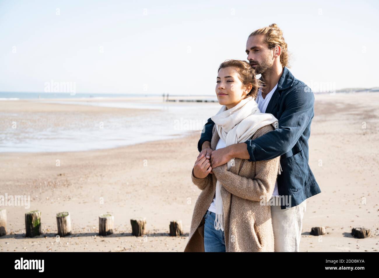 Jeune couple qui regarde loin tout en embrassant à la plage Banque D'Images