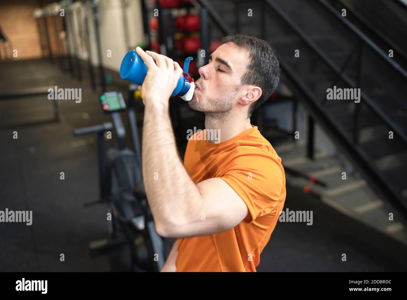 Homme sportif qui boit de l'eau en se tenant dans la salle d'exercice Banque D'Images