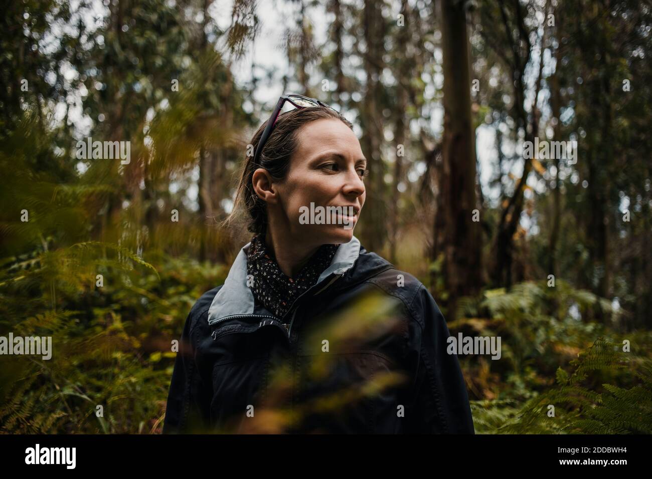 Femme attentionnée regardant loin en se tenant contre les plantes sous la pluie saison Banque D'Images