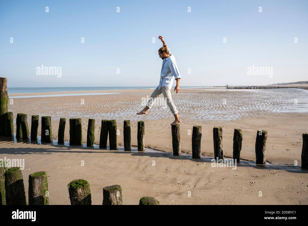 Un jeune homme qui se balance en marchant sur des poteaux en bois à la plage contre le ciel dégagé Banque D'Images