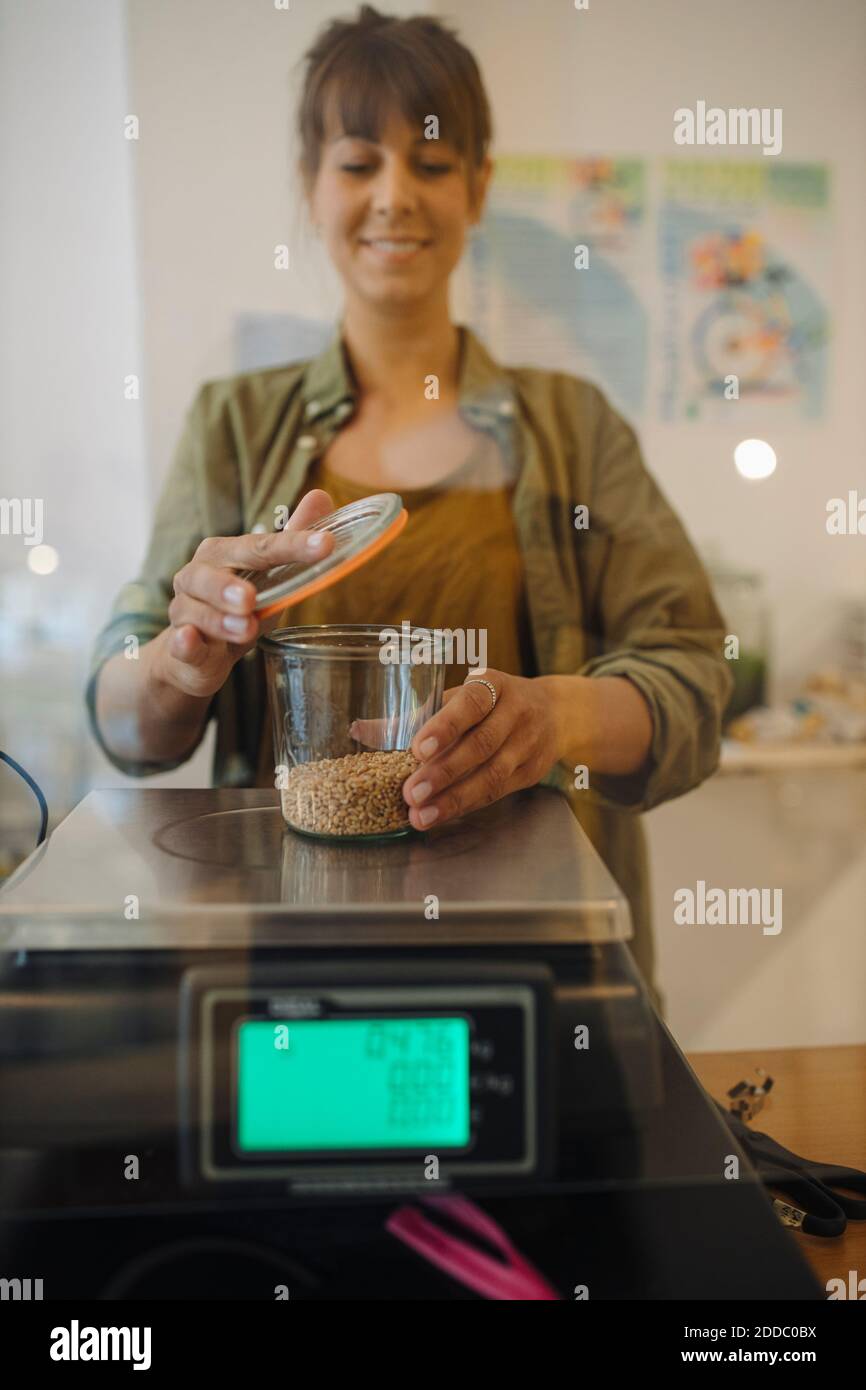 Femme propriétaire pesant le pot à grain sur la balance dans le café Banque D'Images