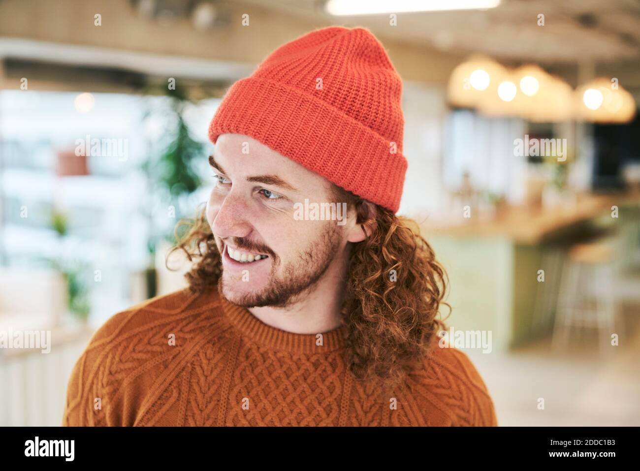 Homme hipster souriant portant un chapeau en tricot rouge à la maison Banque D'Images
