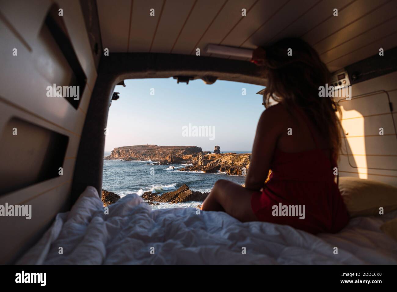 Femme admirant la vue sur la mer en étant assise dans une camionnette de camping à plage Banque D'Images