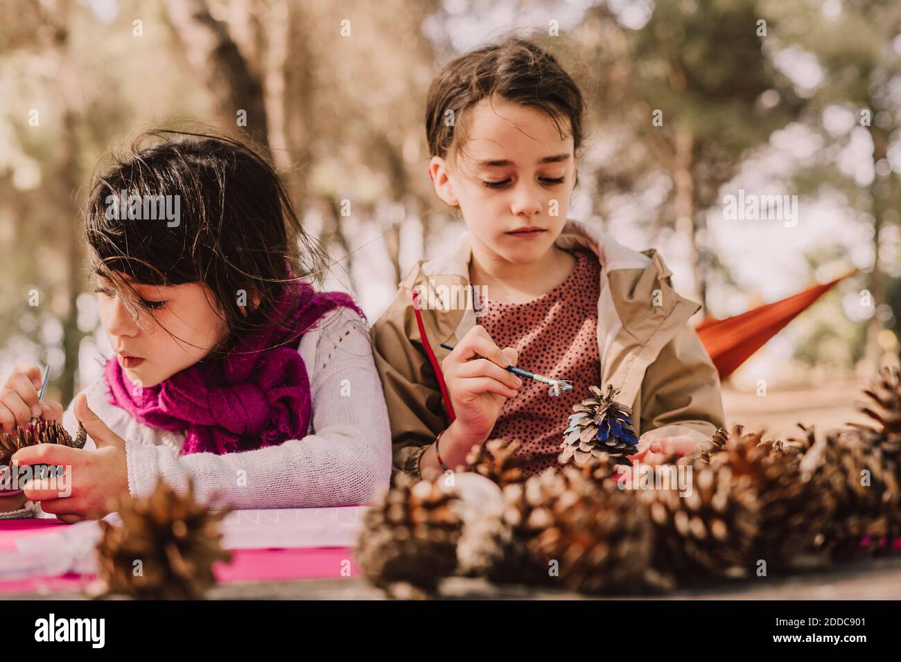 Jolies filles décorant des cônes de pin avec peinture aquarelle à la table dans le parc Banque D'Images