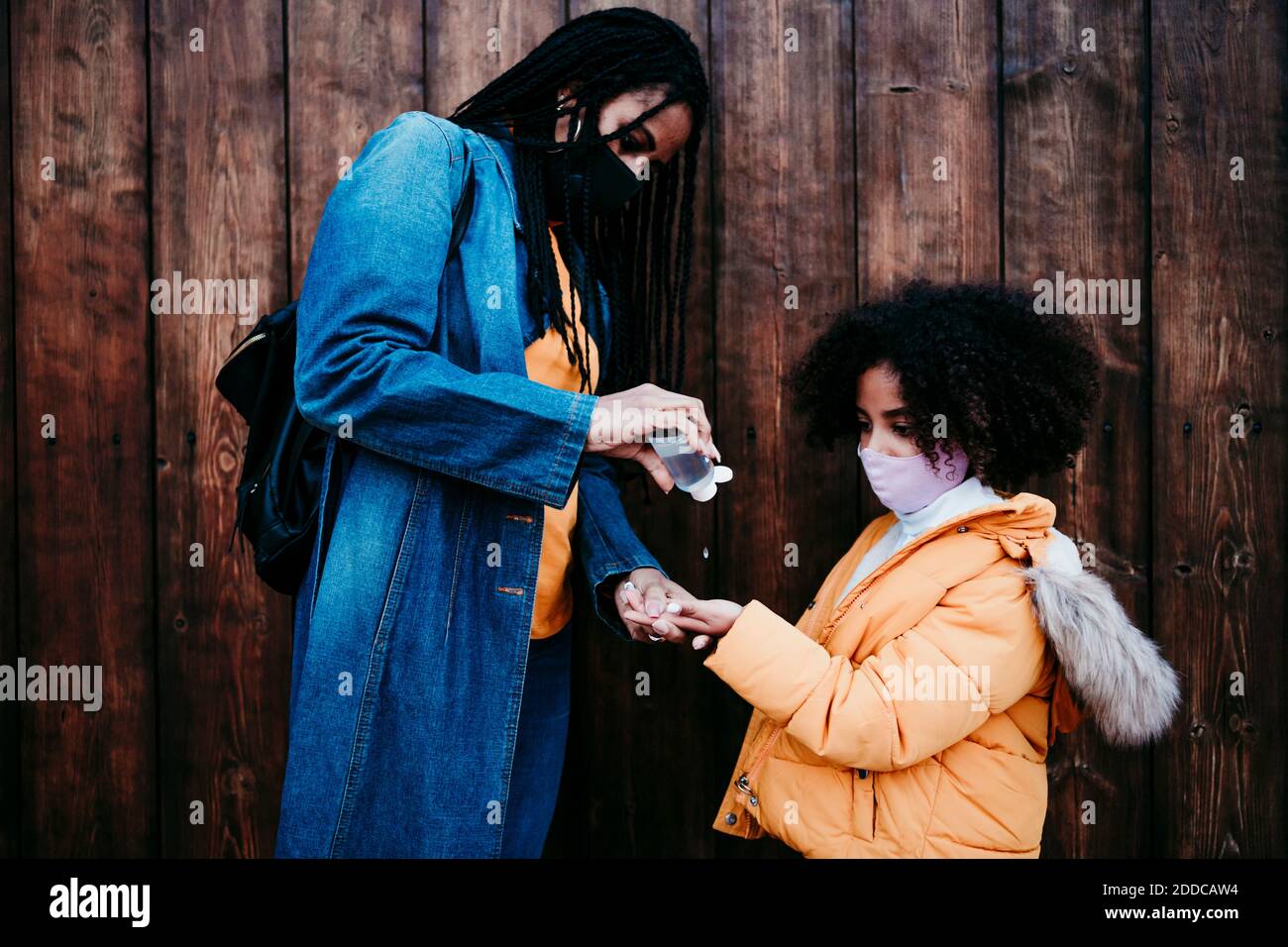 Mère donnant de l'alcool désinfectant pour les mains à la fille tout en se tenant contre mur en bois Banque D'Images