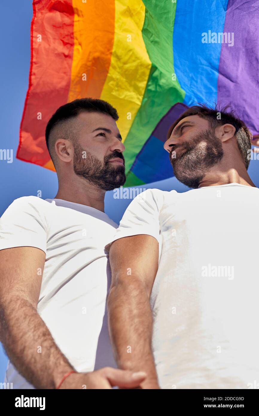 Beau couple gay debout sous le drapeau arc-en-ciel Banque D'Images