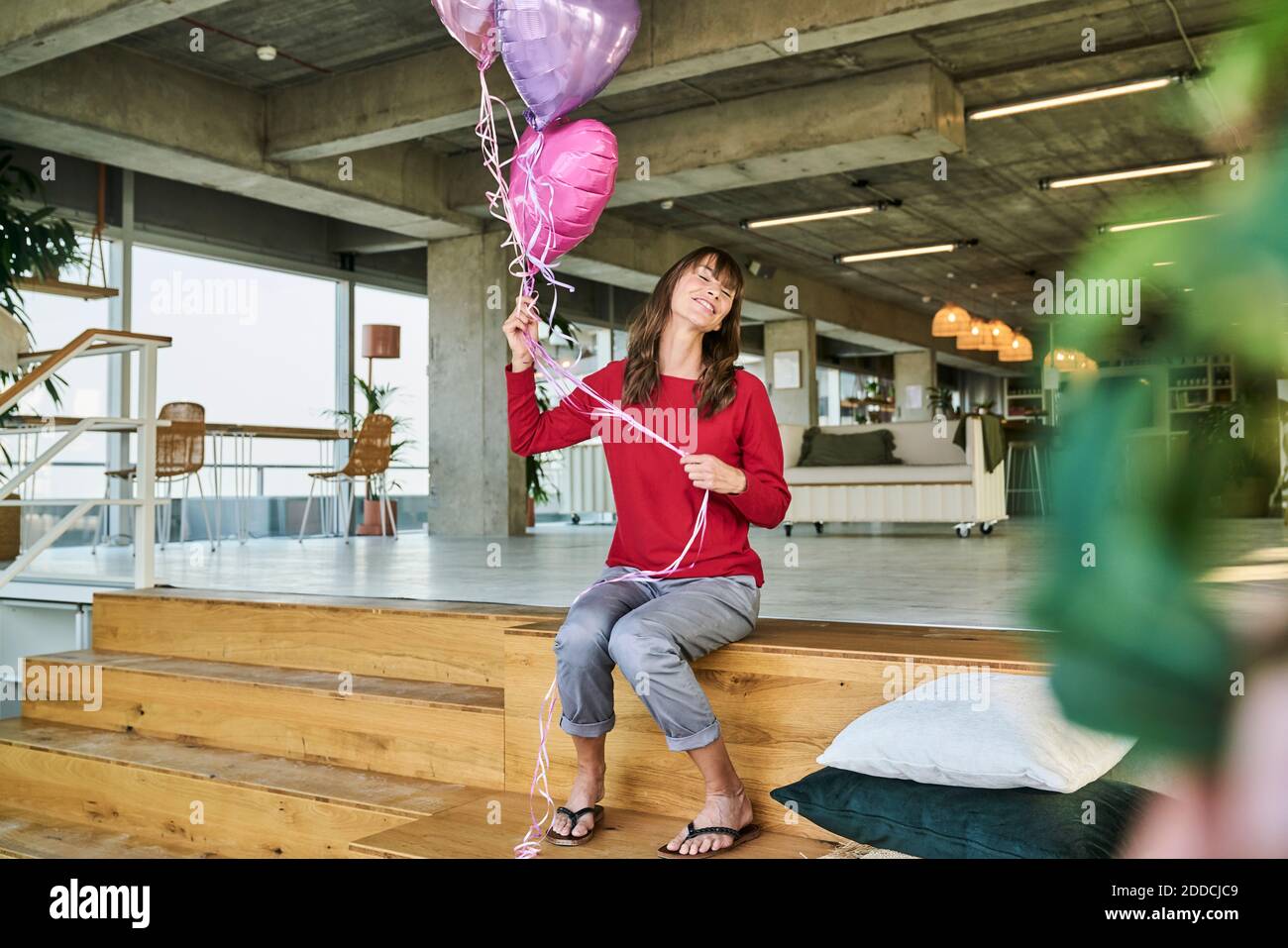 Femme d'affaires tenant des ballons tout en étant assise sur les escaliers dans le bureau de loft Banque D'Images