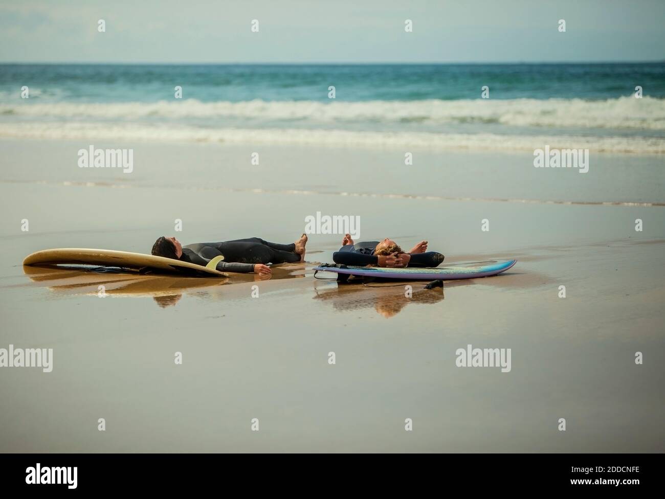 Amis de sexe masculin couchés sur des planches de surf à la plage Banque D'Images