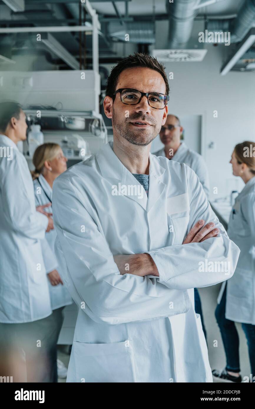 Homme scientifique debout avec les bras croisés et collègue en arrière-plan au laboratoire Banque D'Images