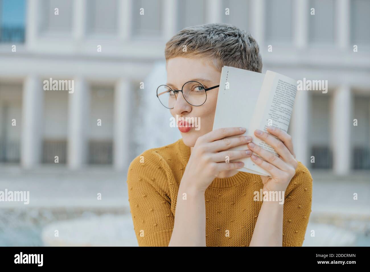 Femme adulte de taille moyenne se cachant le visage avec un livre tout en étant assise jour ensoleillé Banque D'Images