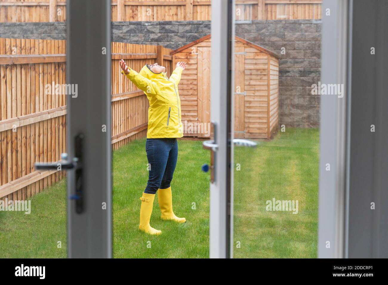 Femme adulte de taille moyenne qui profite de la pluie avec les bras étirés tout en se tenant debout dans la cour arrière pendant la saison des pluies Banque D'Images