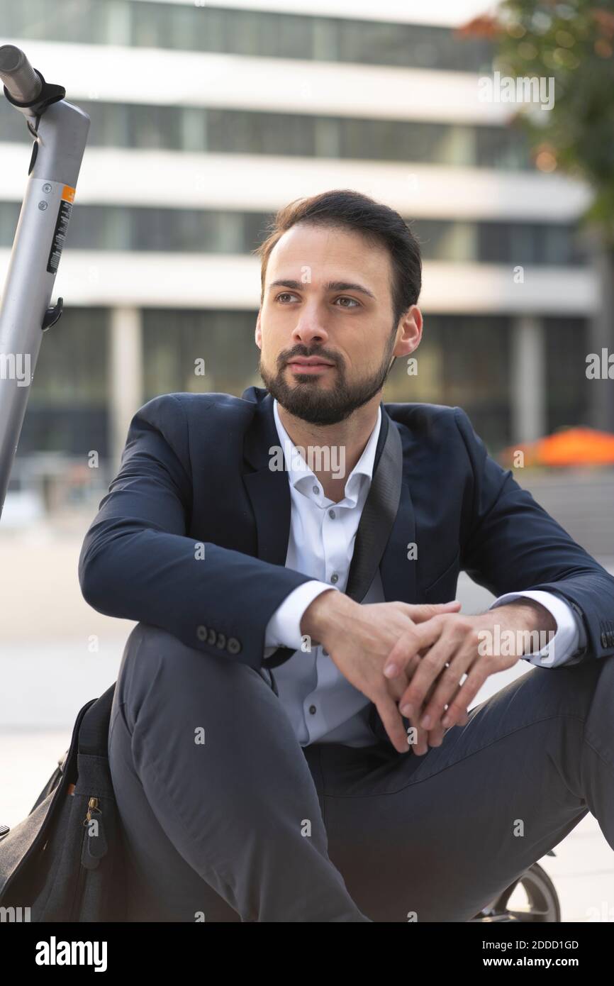 Homme d'affaires confiant sur un scooter électrique assis en ville Banque D'Images