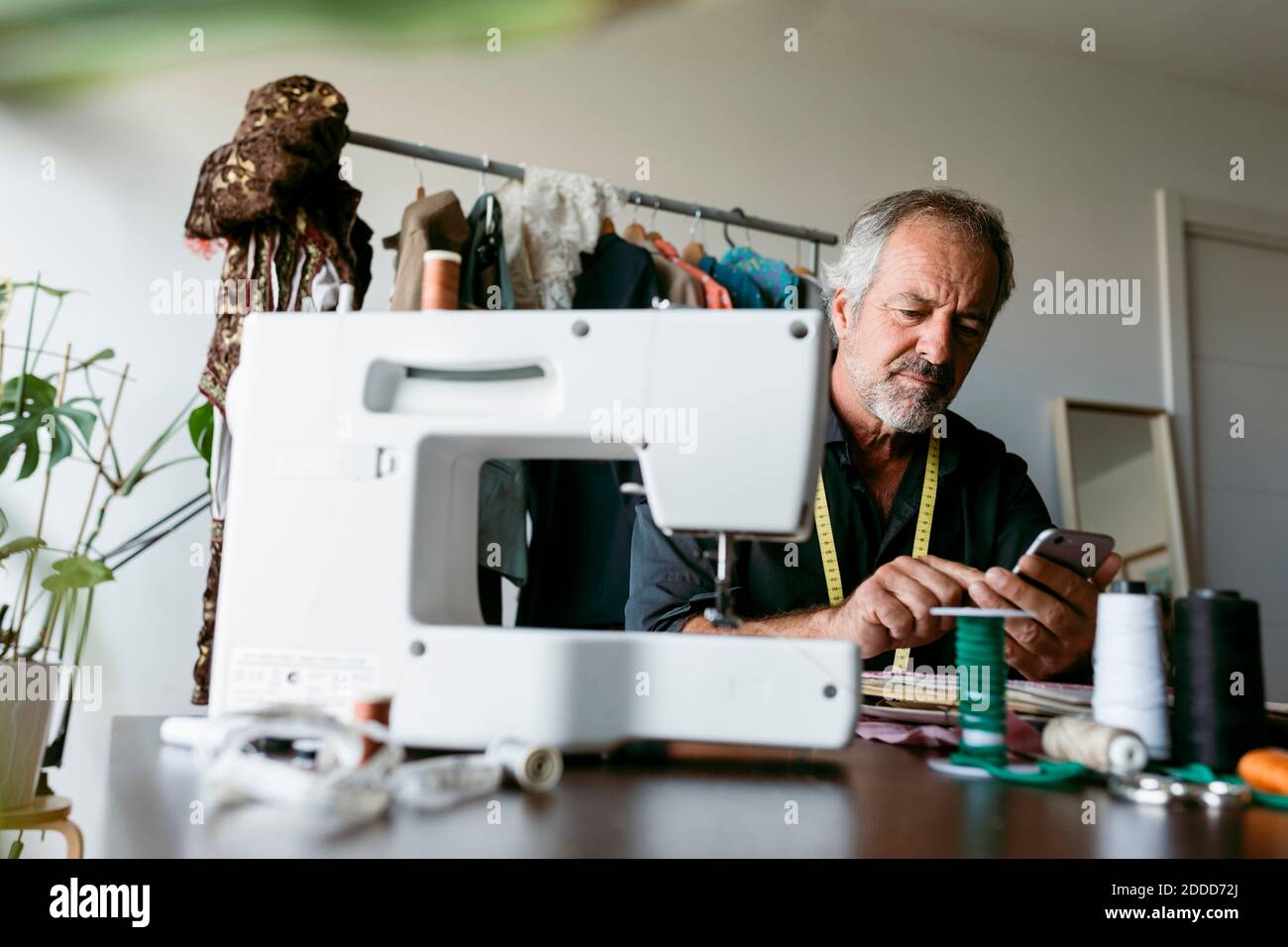 Homme mature sur mesure utilisant un smartphone assis à une table en studio de travail Banque D'Images