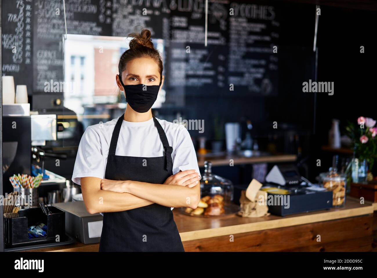 Portrait d'une serveuse dans un masque facial protecteur avec les bras croisés debout au café Banque D'Images