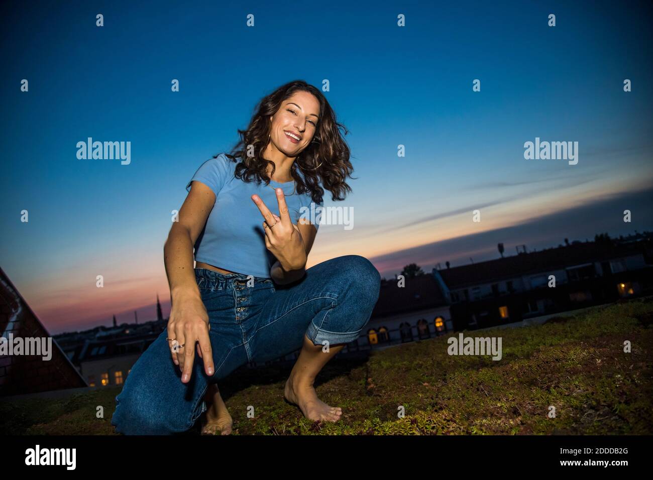 Une jeune femme qui fait la paix signe le geste tout en se croisant sur la construction terrasse au coucher du soleil Banque D'Images