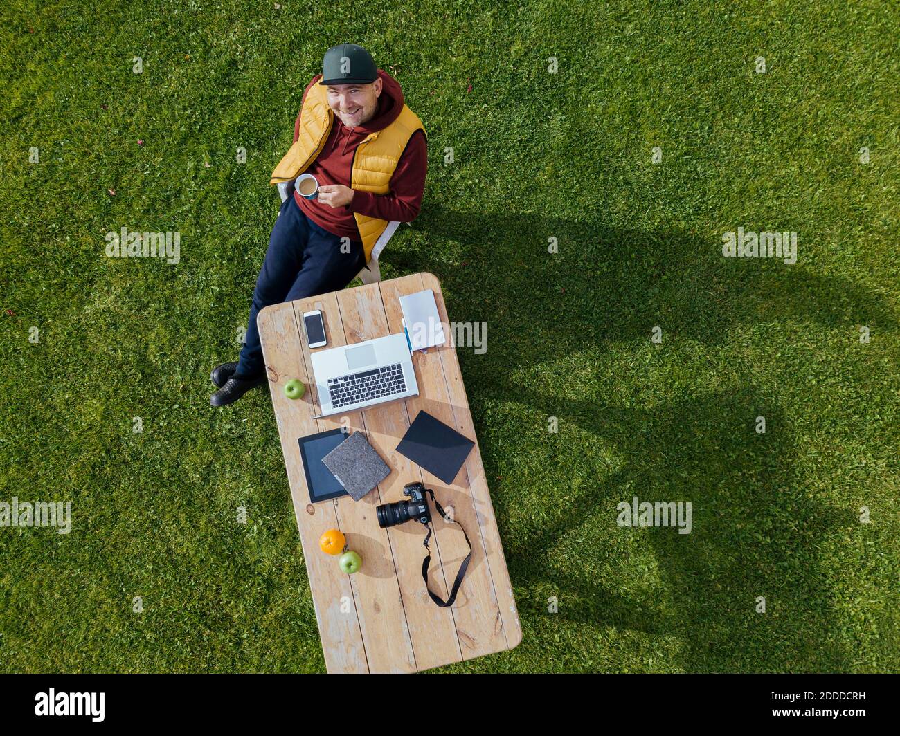 Vue aérienne de l'homme assis à une table basse pelouse verte et sourire à l'appareil photo avec une tasse de café à la main Banque D'Images
