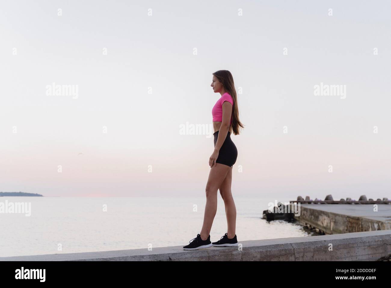 L'athlète admirant la vue sur la mer debout sur le mur de retenue contre clair ciel Banque D'Images