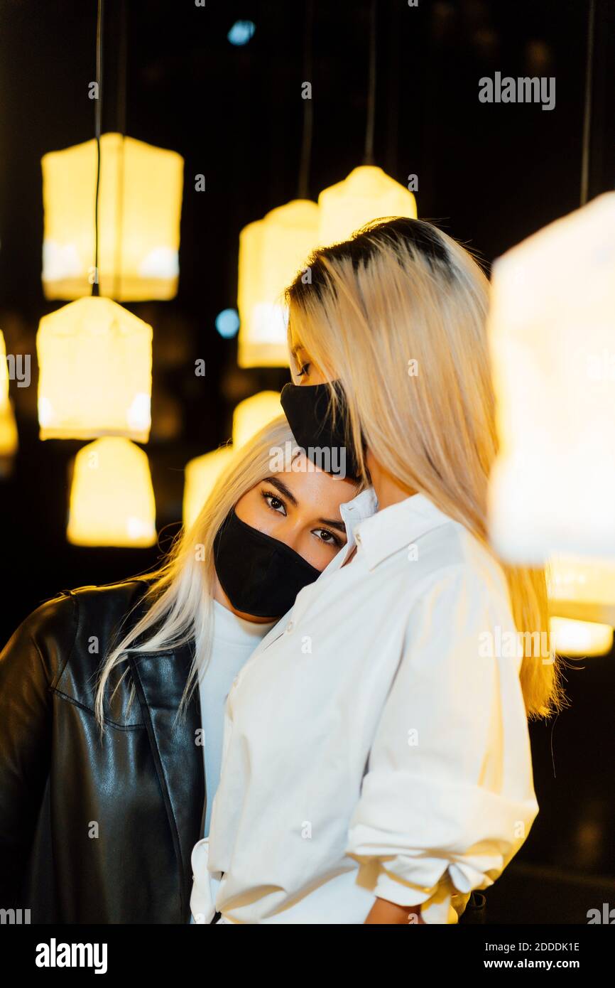 Jeune femme portant un masque facial de protection en gardant la tête sur celle de l'ami tenez-vous debout contre la lampe Banque D'Images