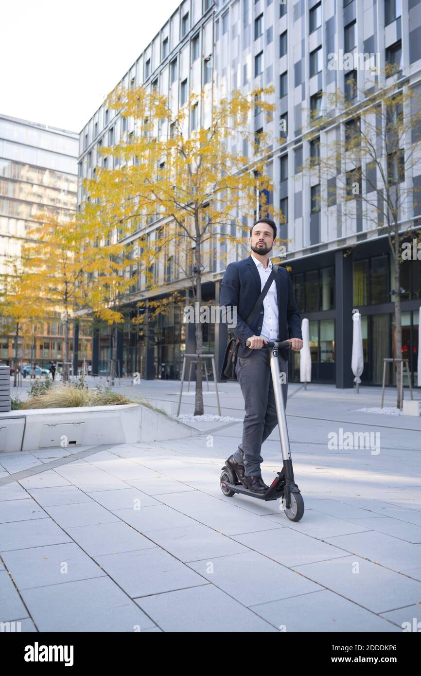 Homme d'affaires à bord d'un scooter électrique contre un bâtiment ville Banque D'Images