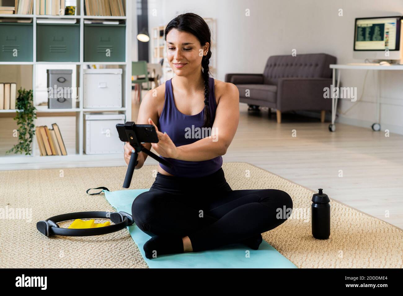 Athlète féminine avec pattes croisées assis sur un tapis d'exercice enregistrement vidéo à la maison Banque D'Images