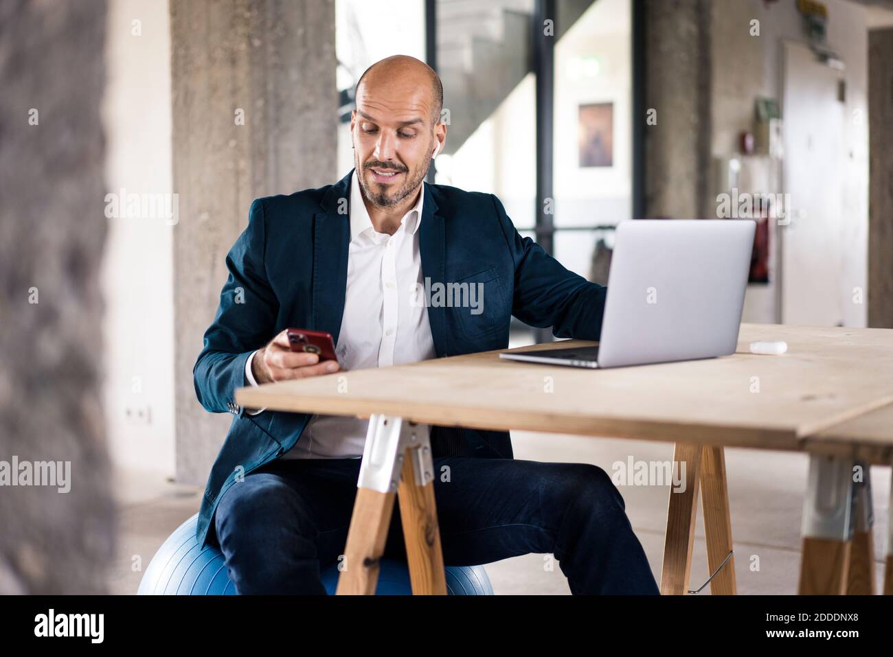 Homme portant une combinaison avec un ordinateur portable et un téléphone portable assis au bureau Banque D'Images