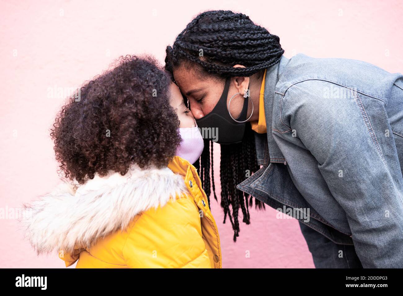 Mère et fille portant un masque facial debout face à face contre le mur rose Banque D'Images