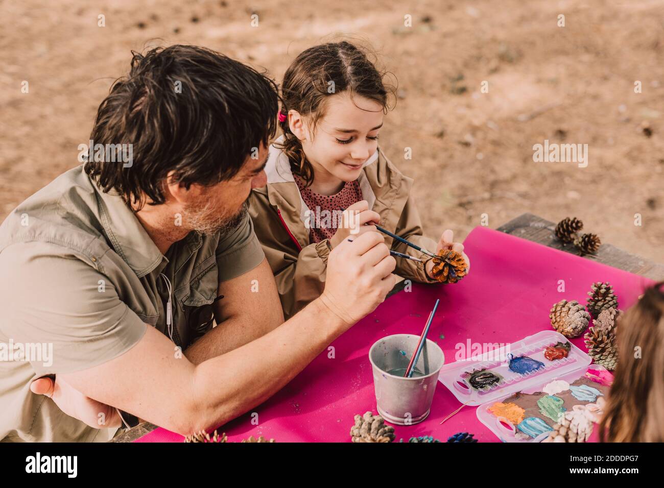 Fille souriante colorant le cône de pin avec le père tout en étant assis à table de pique-nique dans le parc Banque D'Images