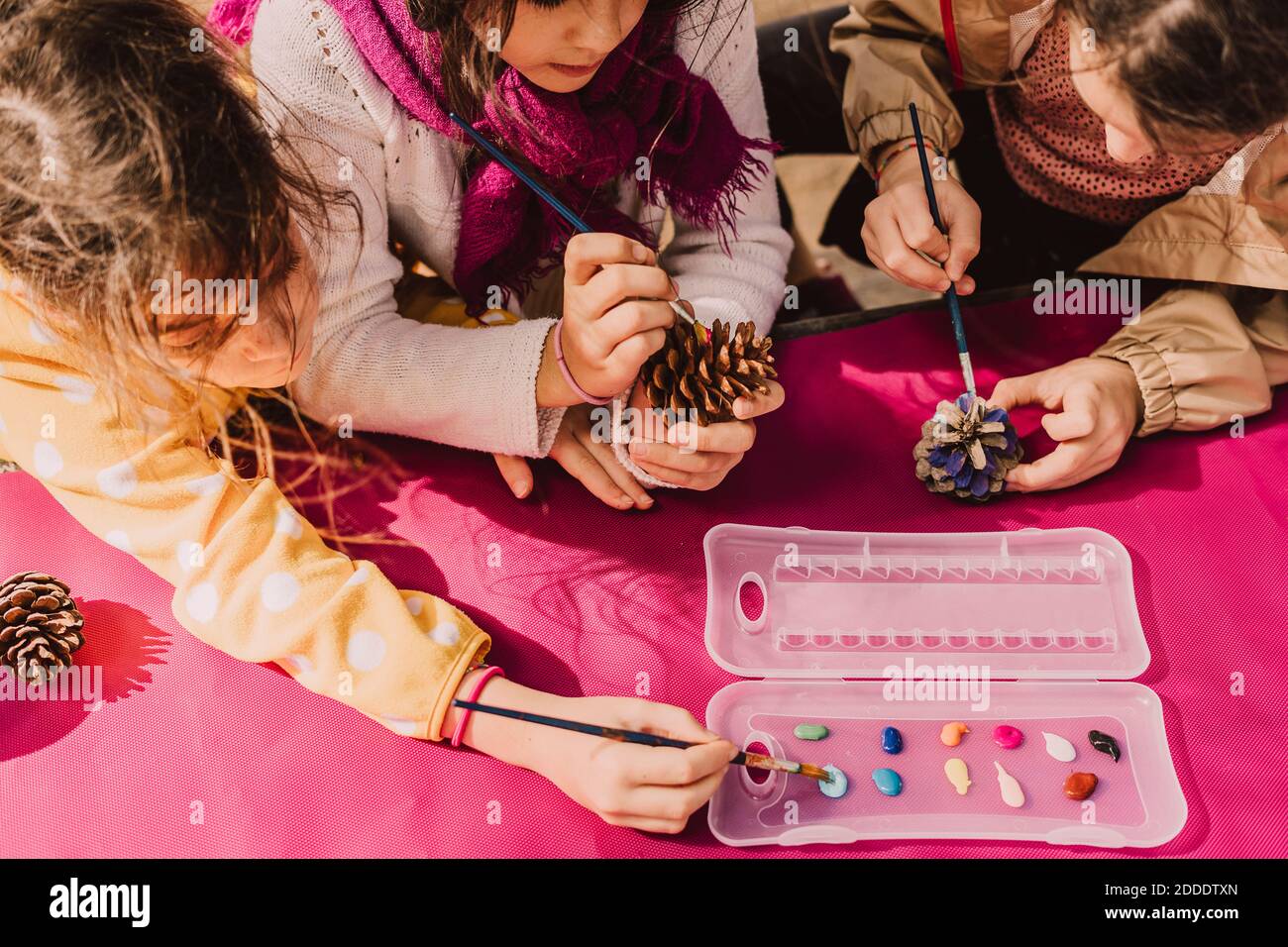 Les filles utilisent des pinceaux pour colorier les cônes de pin à la table de pique-nique dans le parc le jour ensoleillé Banque D'Images