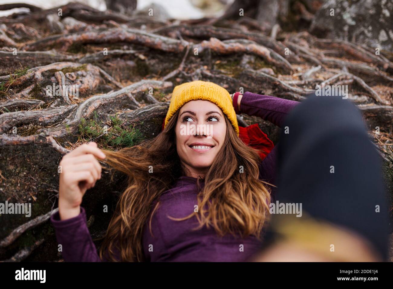 Femme souriante regardant loin en étant allongé sur des racines d'arbres dans la forêt à la Pedriza, Madrid, Espagne Banque D'Images