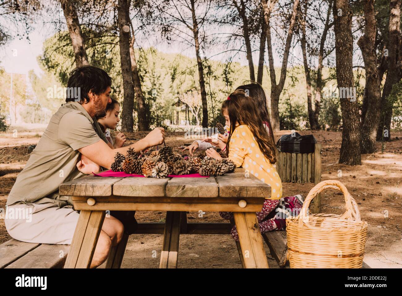 Homme mature avec des filles colorant des cônes de pin à la table de pique-nique dans le parc Banque D'Images