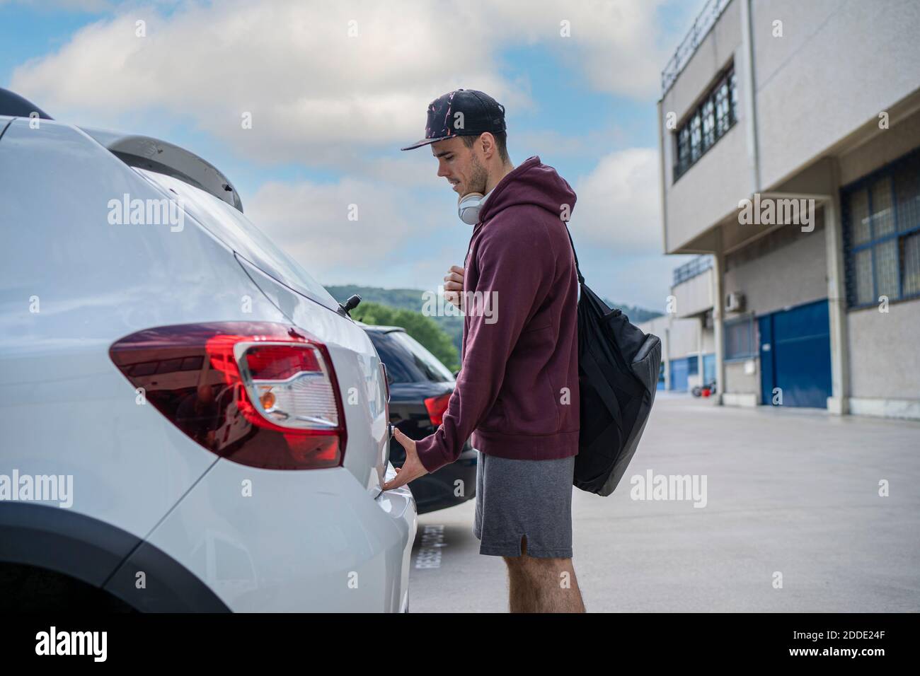 Homme adulte de taille moyenne ouvrant le coffre de la voiture en se tenant au parking lot Banque D'Images