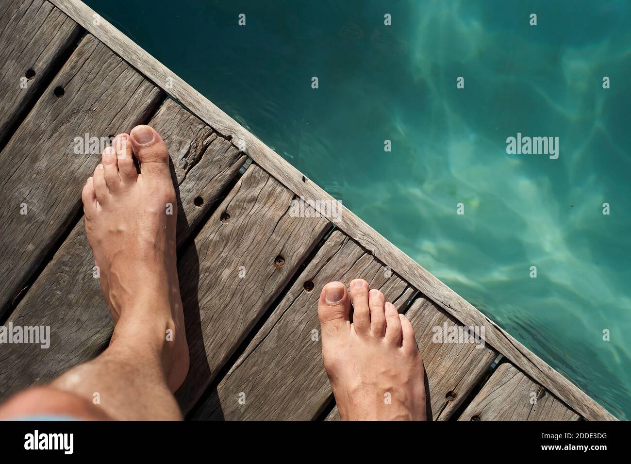 Les pieds de l'homme sur le plancher près de la piscine pendant la journée ensoleillée Banque D'Images