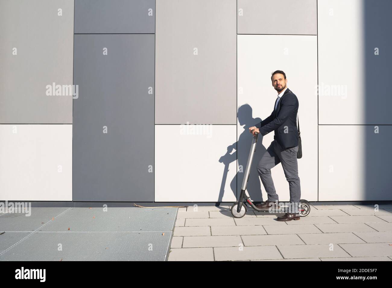 Homme d'affaires à bord d'un scooter électrique contre un mur dans la ville Banque D'Images