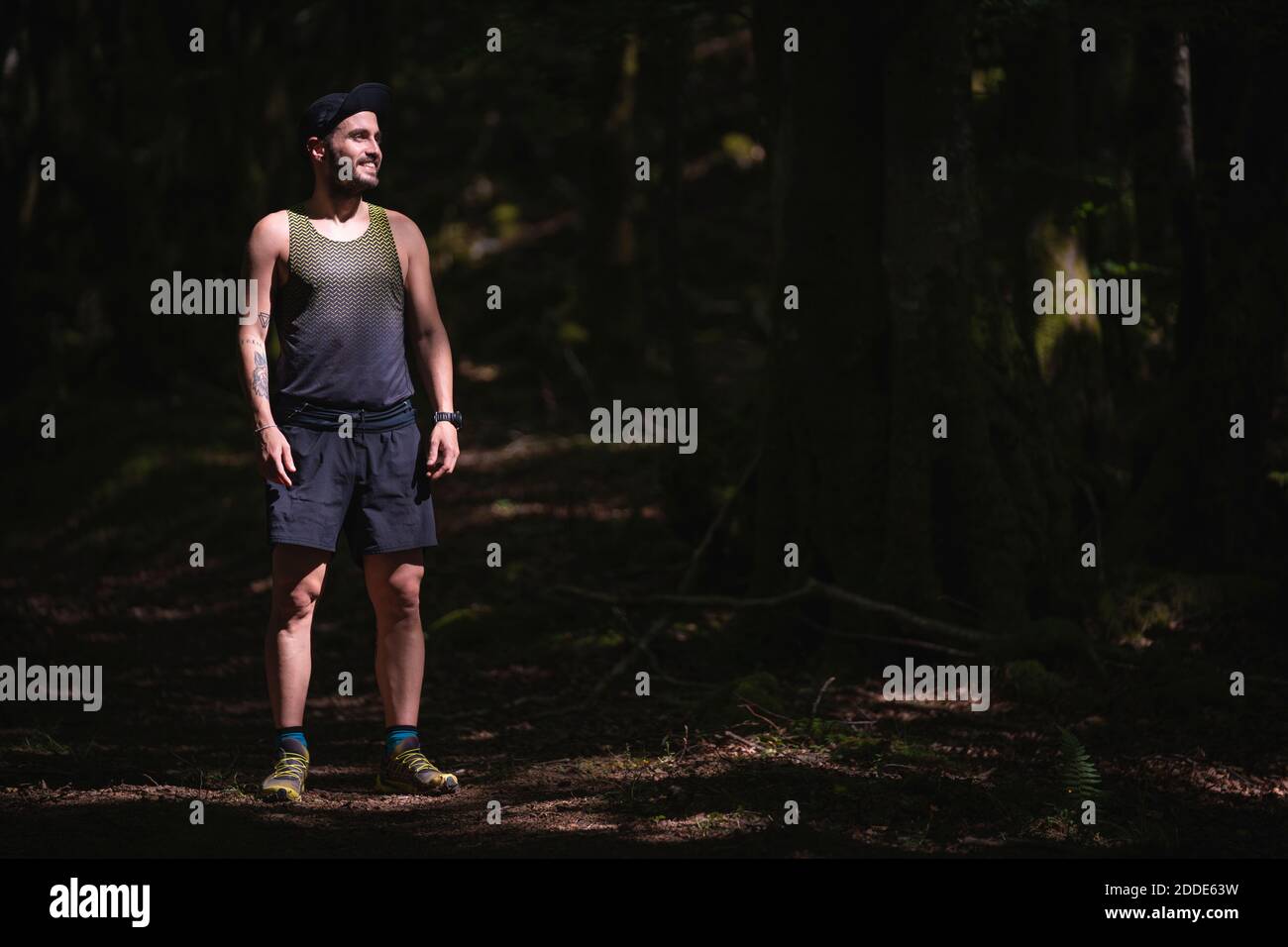 Homme souriant portant des vêtements de sport regardant loin en se tenant debout forêt Banque D'Images