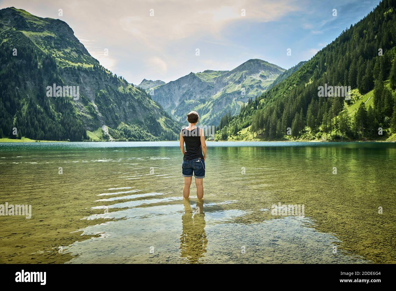 Femme mûre debout genou profondément dans Vilsalpsee tout en regardant chaîne de montagnes par beau temps Banque D'Images