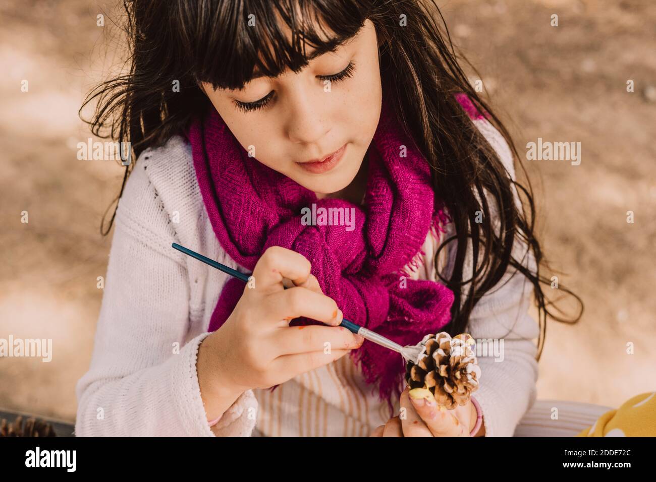 Jolie fille colorant le cône de pin avec pinceau au parc Banque D'Images