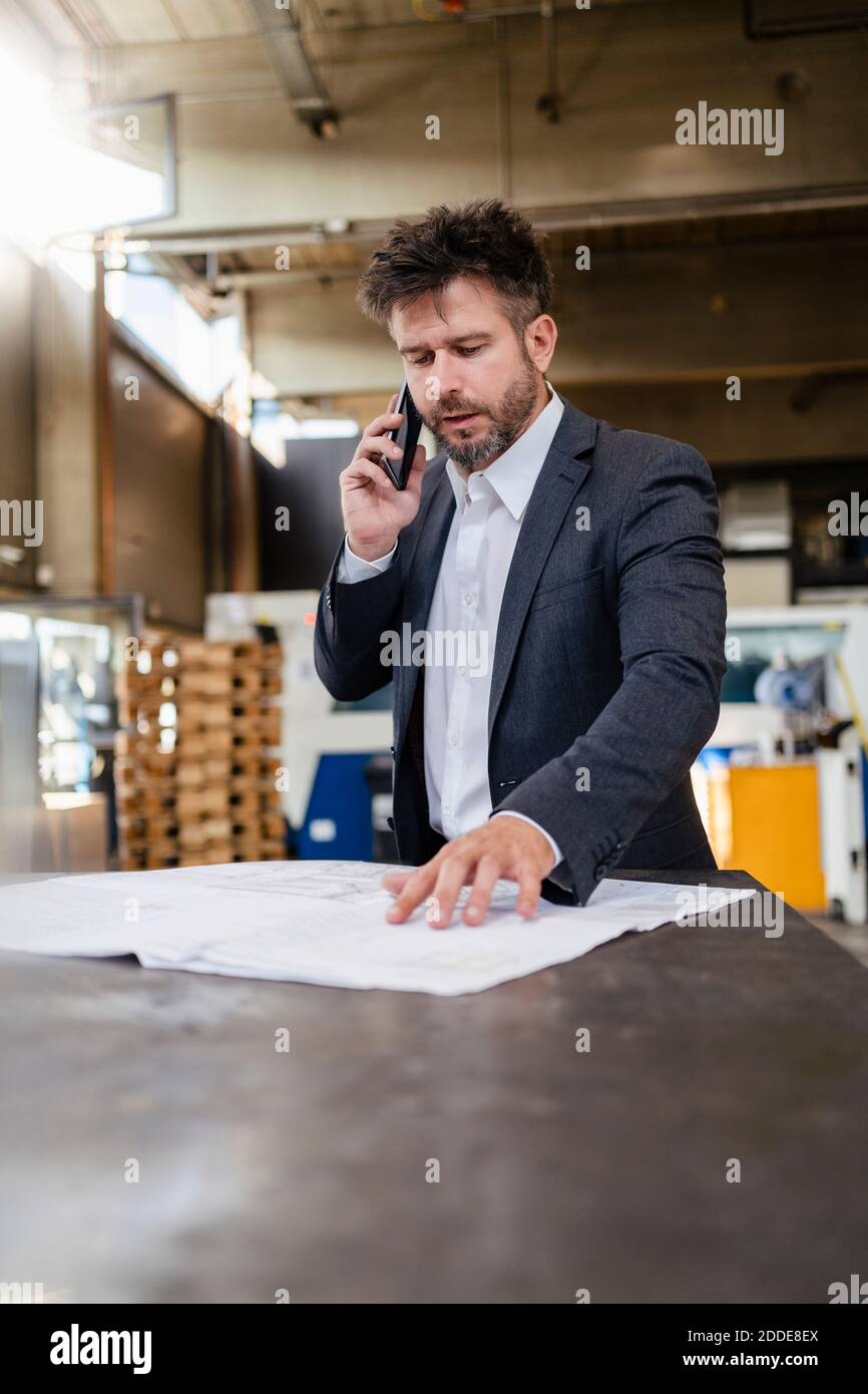 Homme d'affaires vêtu d'un costume qui parle sur un téléphone portable tout en travaillant usine Banque D'Images
