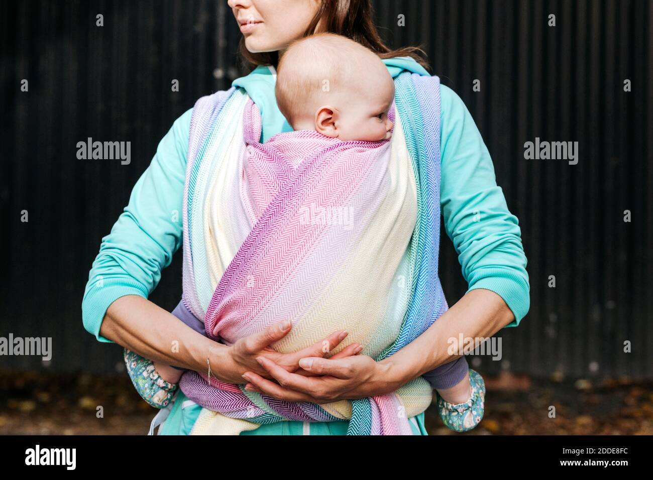 Section médiane mère transportant le bébé enveloppée dans une couverture debout contre du métal mur Banque D'Images