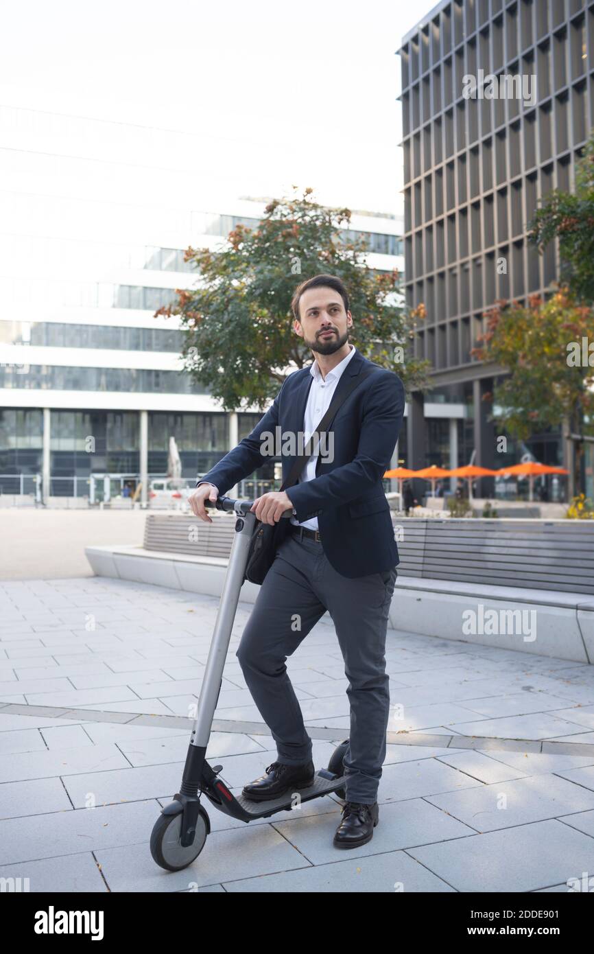 Homme d'affaires avec scooter électrique contre bâtiment dans la ville Banque D'Images