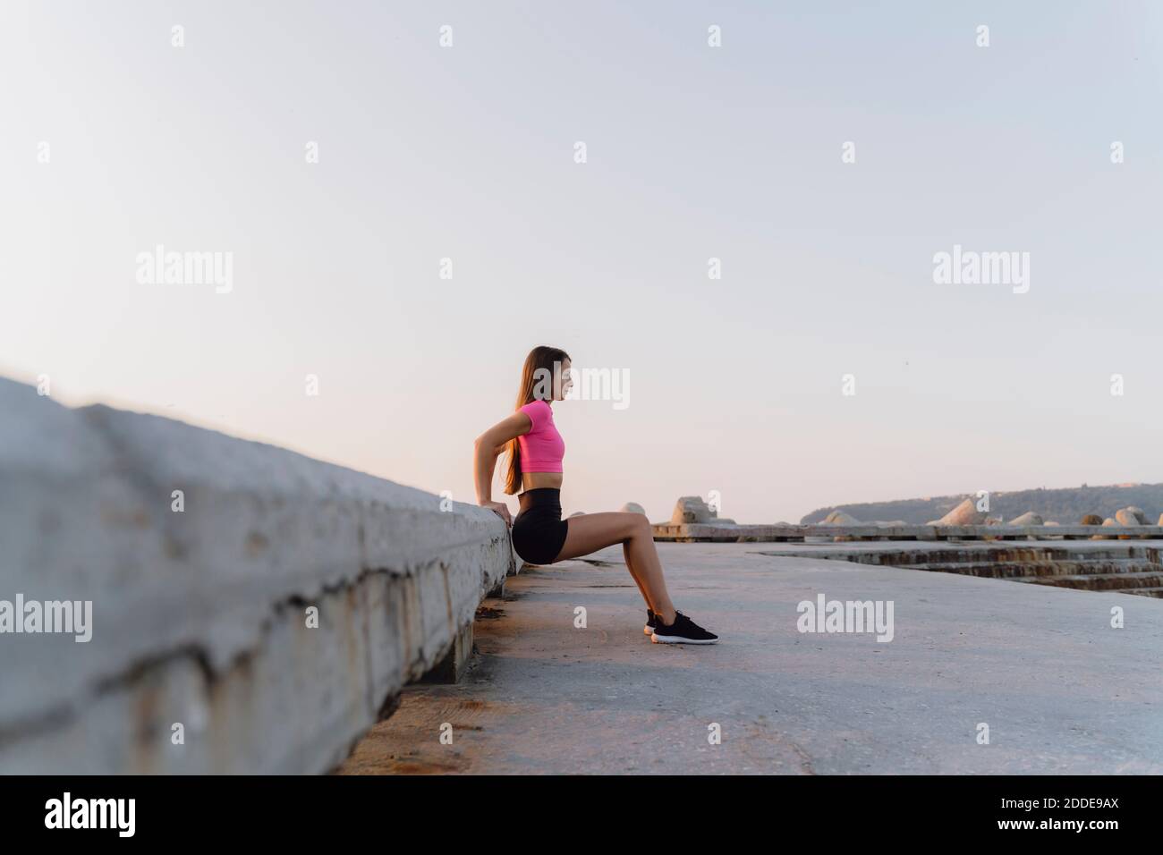 Femme s'exerçant tout en se penchant sur le mur contre le ciel clair Banque D'Images